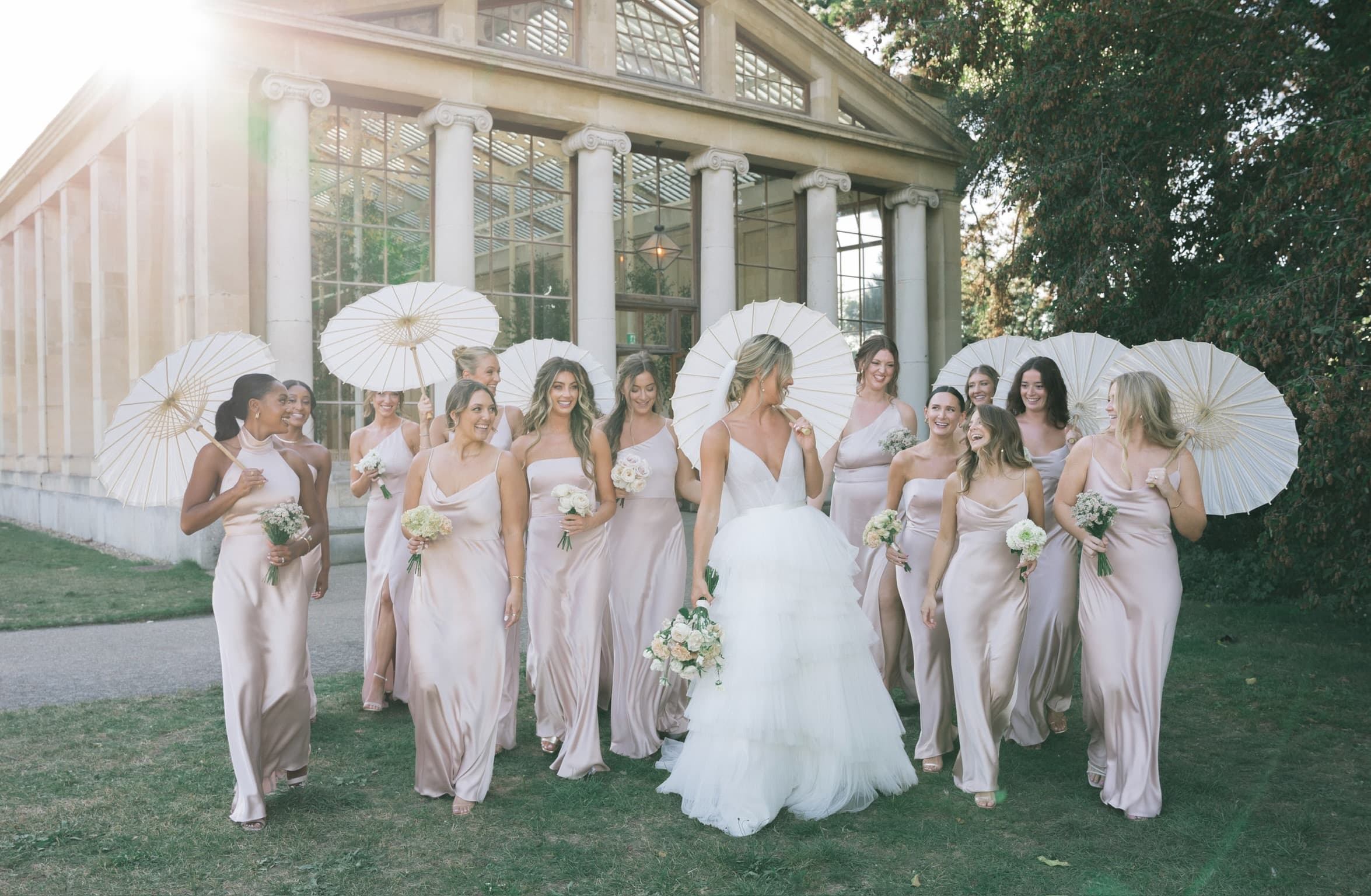 Bride and bridal party walking with parasols outside a wedding venue